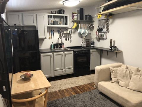 A kitchen with a black fridge, white cabinets, and a wooden table with a bowl of fruit on it.