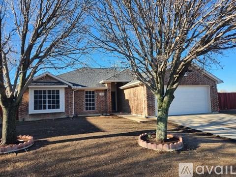 A house with a white garage door and a brick exterior is surrounded by bare trees.