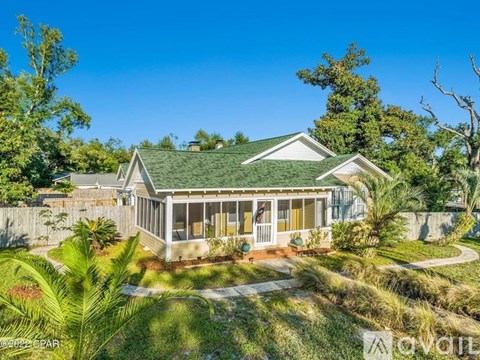 A house with a green roof and a porch surrounded by greenery.