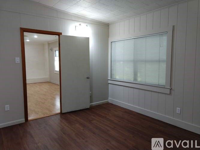 A room with a wooden floor and white walls, with a door leading to another room.