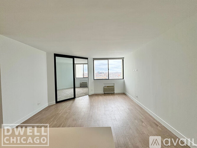 A spacious room with wooden floors and a large window overlooking a cityscape.