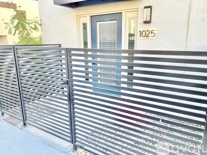 A metal fence with horizontal slats in front of a house with the number 1025 on it.