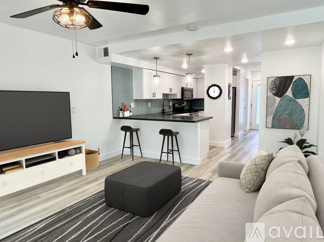 A modern living room with a flat screen TV, bar stools, and a kitchen area in the background.