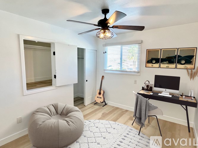 A room with a ceiling fan, a chair, a desk, and a guitar.