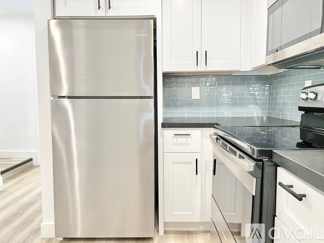 A stainless steel refrigerator stands in a kitchen with white cabinets and a black stove.