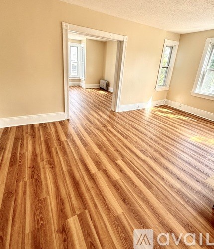 A room with wooden flooring and two windows.