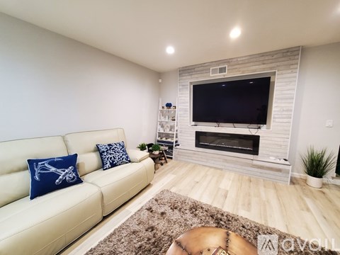 A living room with a white couch and a flat screen TV mounted on a brick wall.