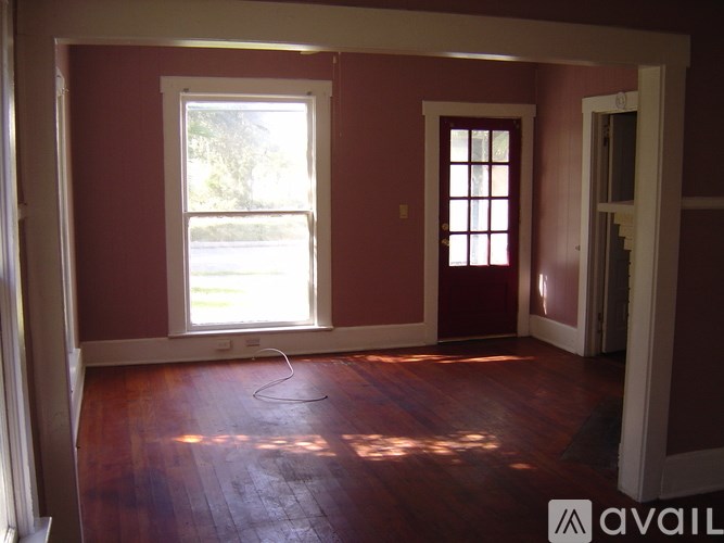 A room with red walls and wooden floors with a window and a door.