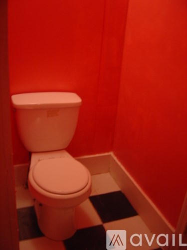 A white toilet in a bathroom with red walls and a black and white checkered floor.