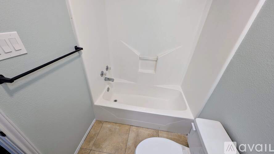 A white bathtub is in a bathroom with a toilet and a towel bar.