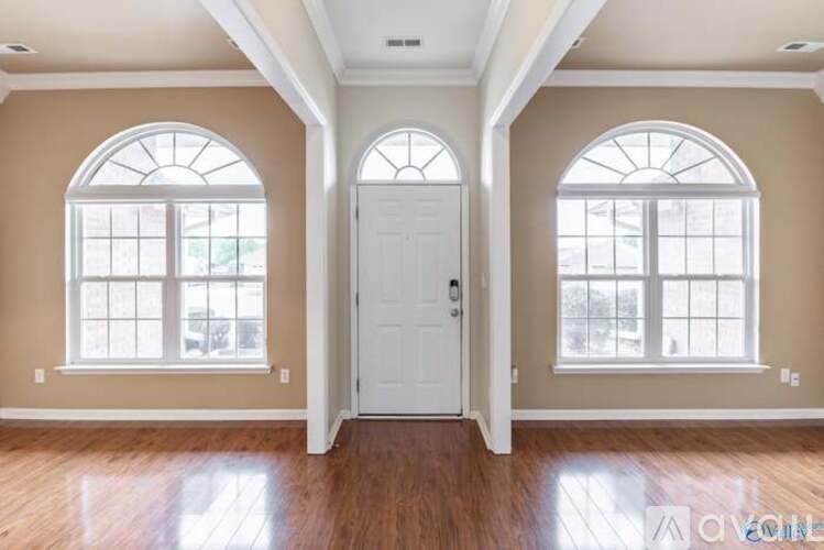 A room with a white door and two windows with wooden floors.
