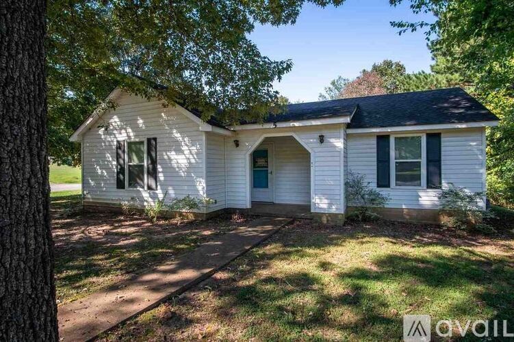 A white house with a black roof and a tree in front.