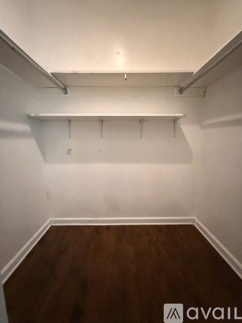 A room with white walls and wooden floors with a white shelf and a few hooks.