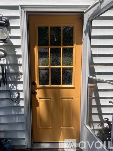 A yellow door with a glass window is on a white house.