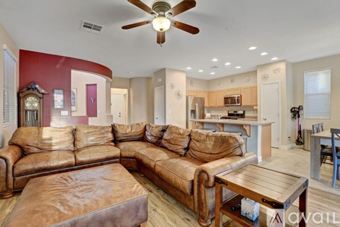 A living room with a brown leather couch and a ceiling fan.