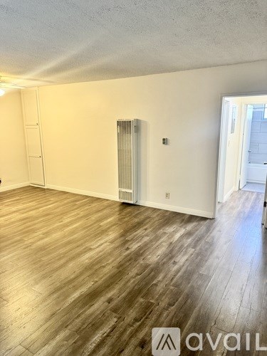 A room with wooden flooring and a white wall with a window.