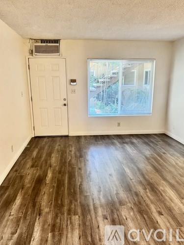 A room with wooden flooring and a window overlooking a fence.