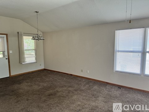 A room with a carpeted floor, a chandelier, and a window with blinds.