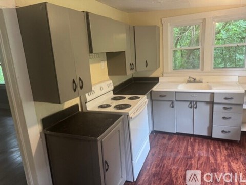 A kitchen with a white stove top oven and a black trash bin.