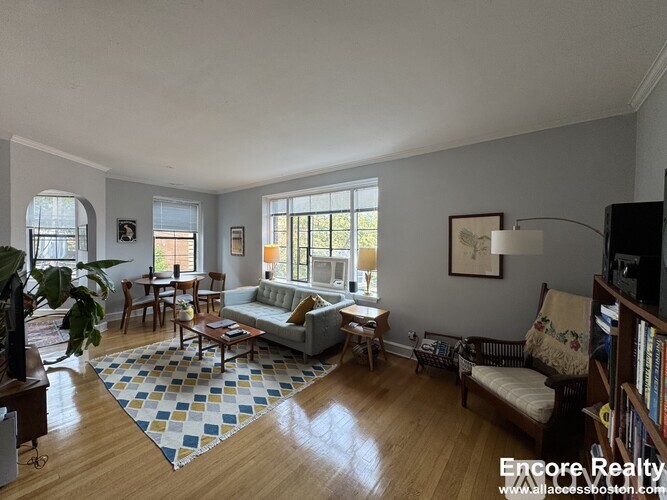 A sunny living room with a couch, chairs, and a rug.