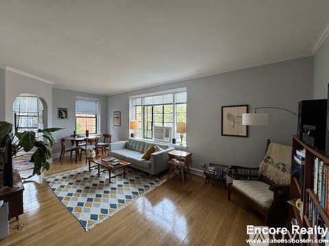 A sunny living room with a couch, chairs, and a rug.