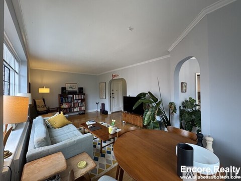 A well-lit living room with a grey couch, a wooden table, and a bookshelf.