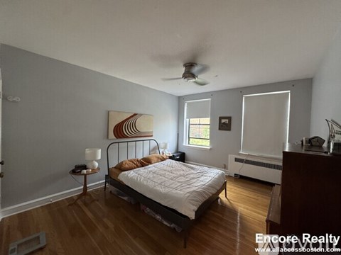 A bedroom with a bed, a ceiling fan, and a painting on the wall.