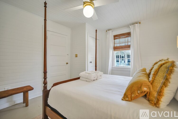 A bedroom with a four poster bed and a window with white curtains.