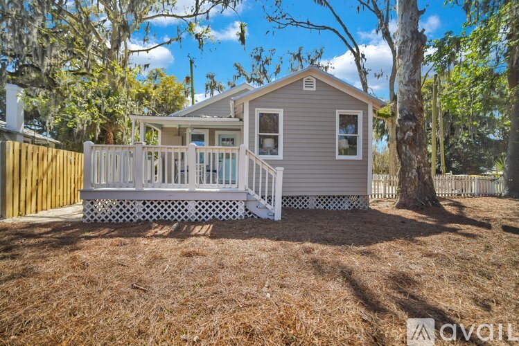 A small house with a porch is surrounded by trees and has a wooden fence.