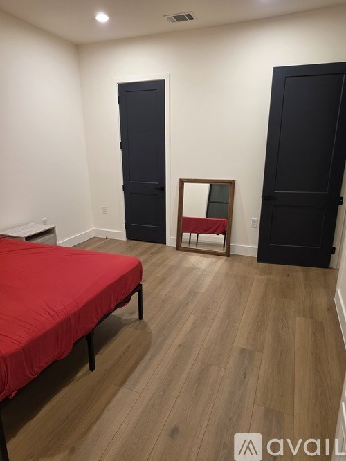 A bedroom with a red bedspread and a wooden floor.