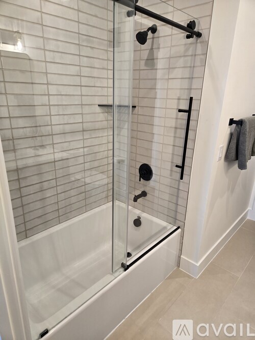 A white tiled shower with a glass door and a black handle.