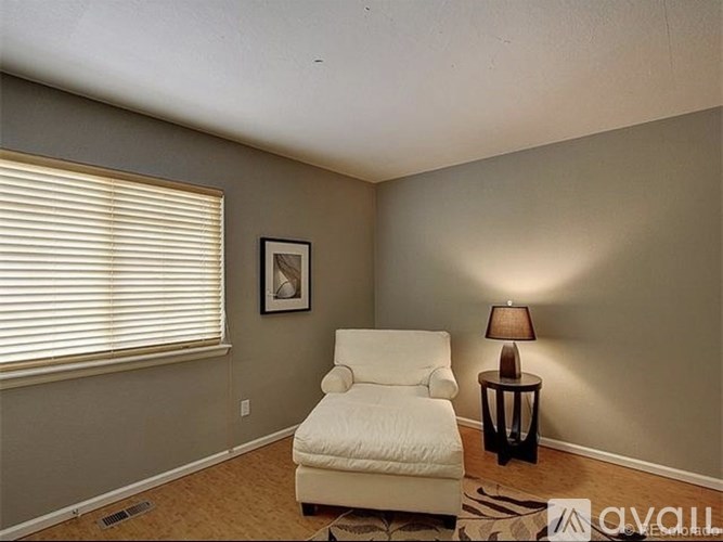 A white chair is in a room with a window and a picture on the wall.