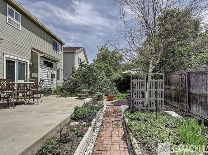 A backyard with a brick pathway and a wooden fence.