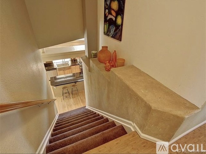 A staircase with a wooden handrail and steps leading to a room with a window and a painting on the wall.