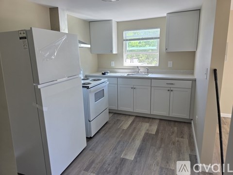 A white refrigerator stands in a kitchen with wooden floors and white cabinets.