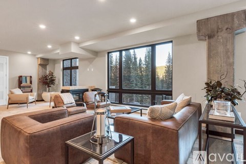 A living room with brown leather furniture and a large window overlooking a forest.