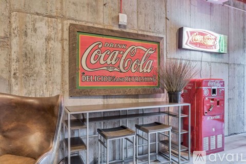 A Coca-Cola vending machine sits next to a table with a metal chair.