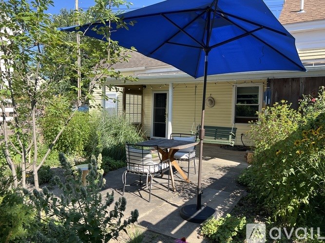 A blue umbrella is on a patio table with chairs.