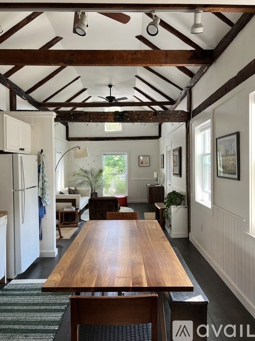 A long wooden table is in the middle of a room with a white fridge on the left.