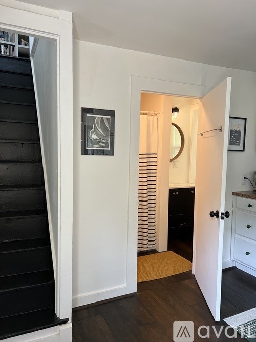 A hallway with a black staircase and a white door leading to a kitchen.