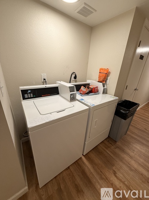 A room with wooden floors and a kitchen area in the background.
