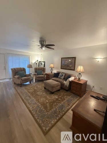 A living room with a rug, a couch, a chair, a side table with a lamp, and a ceiling fan.