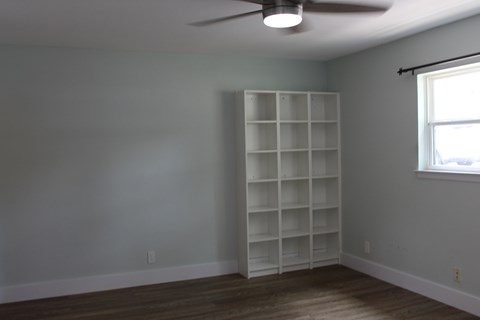 A room with a white bookshelf and a ceiling fan.