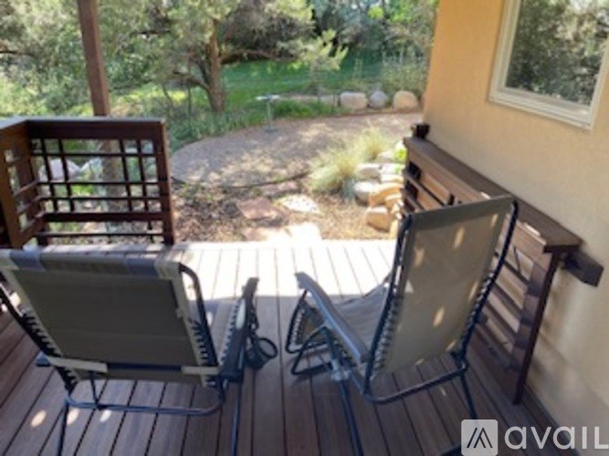 Two chairs are on a wooden deck with a view of a garden.