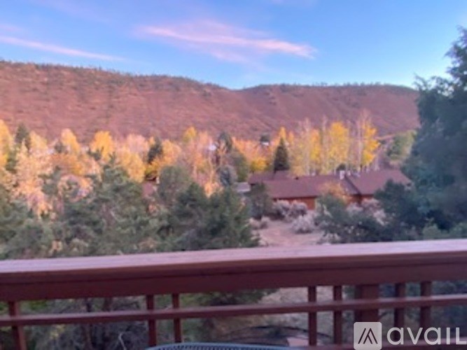 A mountain landscape with a house and trees in the foreground.