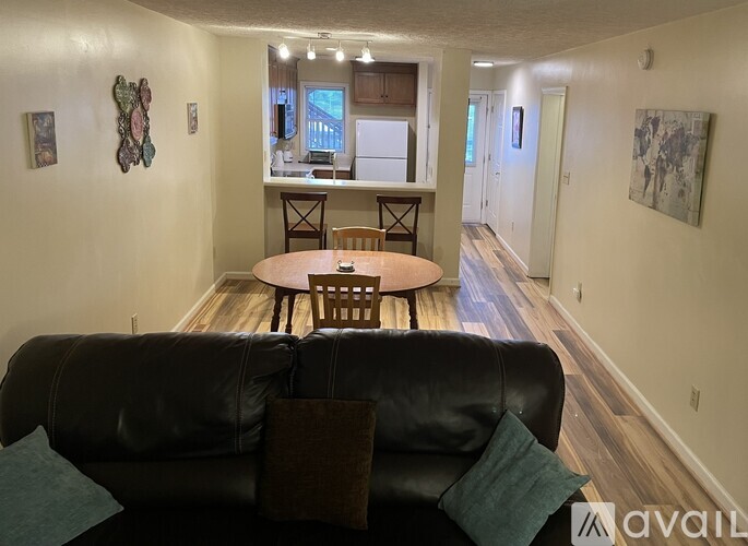 A black couch with a green pillow is in the foreground of a living room with a dining table and chairs.