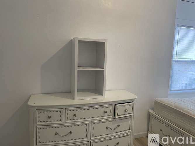 A white shelf unit with drawers is on top of a white dresser.