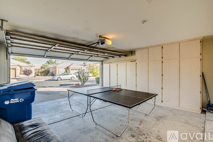A table tennis table is in a garage with a blue trash can and a broom.