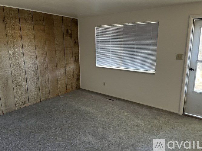 A room with a window covered by blinds and a door on the right side.