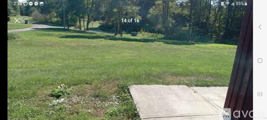 A grassy field with a concrete pathway and trees in the background.